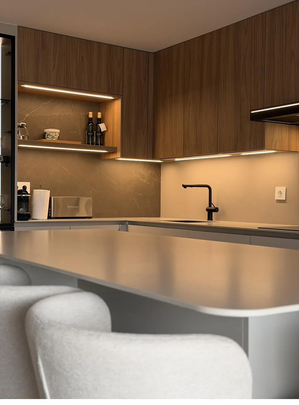 Detalle de una cocina a medida con frentes de madera, iluminación cálida y encimera clara