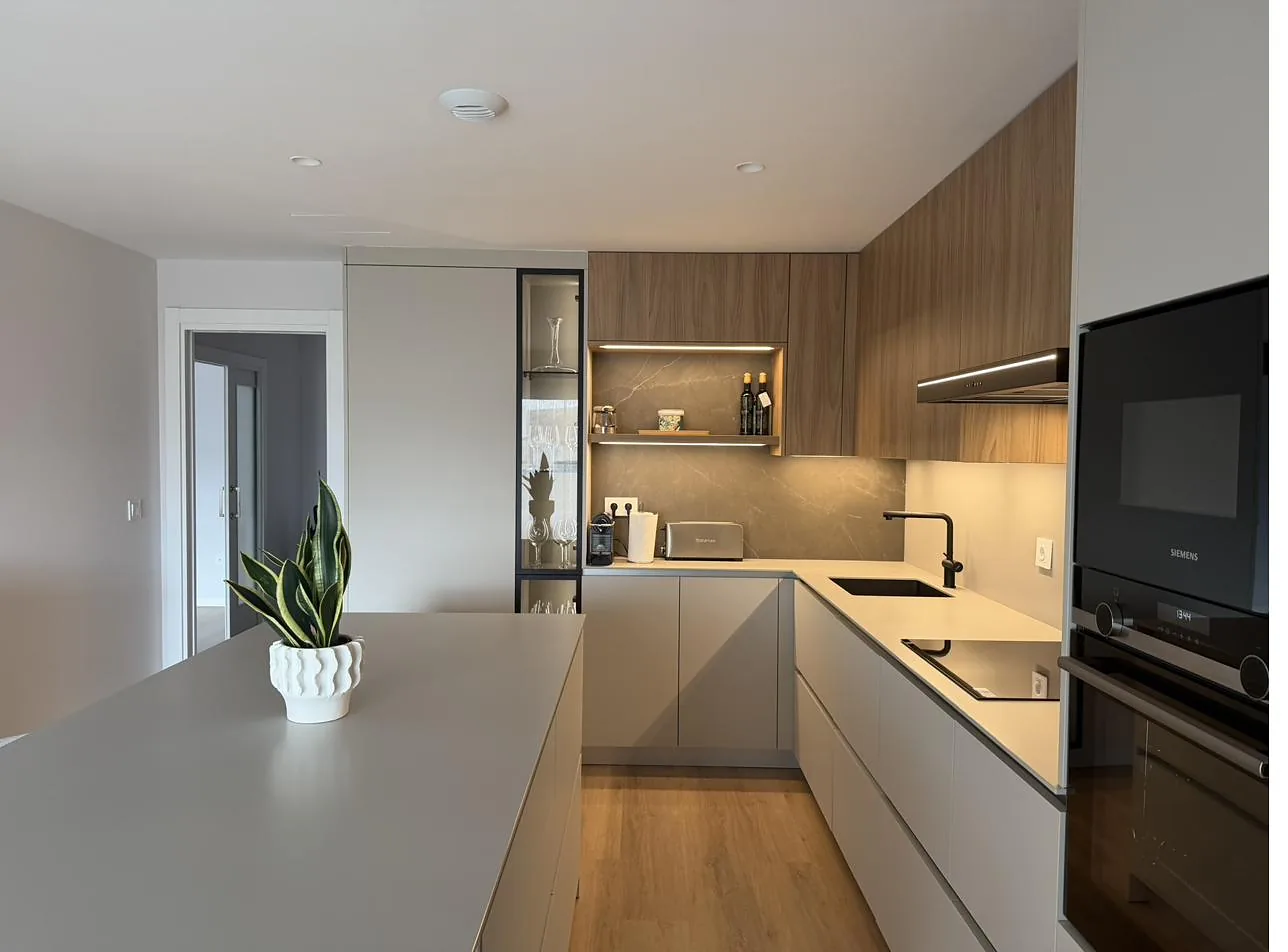 Cocina abierta con isla, frentes claros y muebles altos de madera