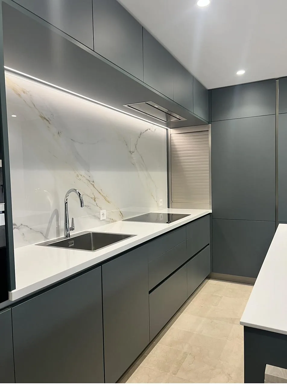 Cocina a medida en tono verde grisáceo con encimera clara y frente de gran formato